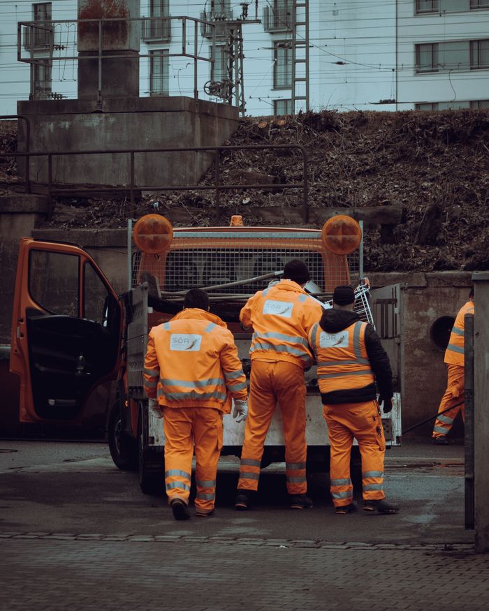 about-us Group of construction workers in orange safety uniforms at a job site in a city.