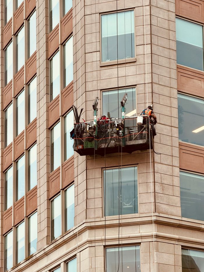 our-story Window cleaners working on suspended platform against a Boston skyscraper. Safety equipment visible.