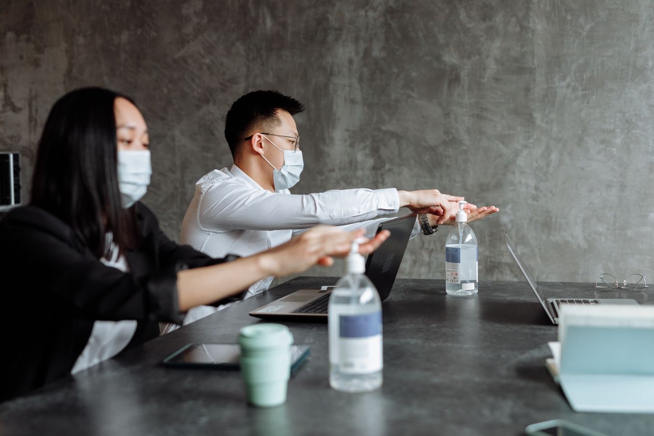 who-we-are Office workers using sanitizer with masks, emphasizing pandemic safety measures.
